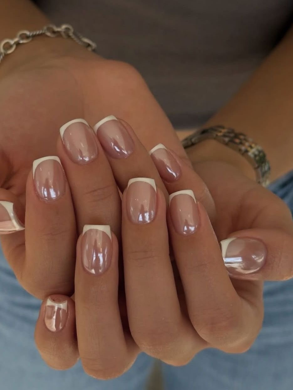 Close-up of a hand displaying a classic French manicure with white tips and glossy nude nail polish