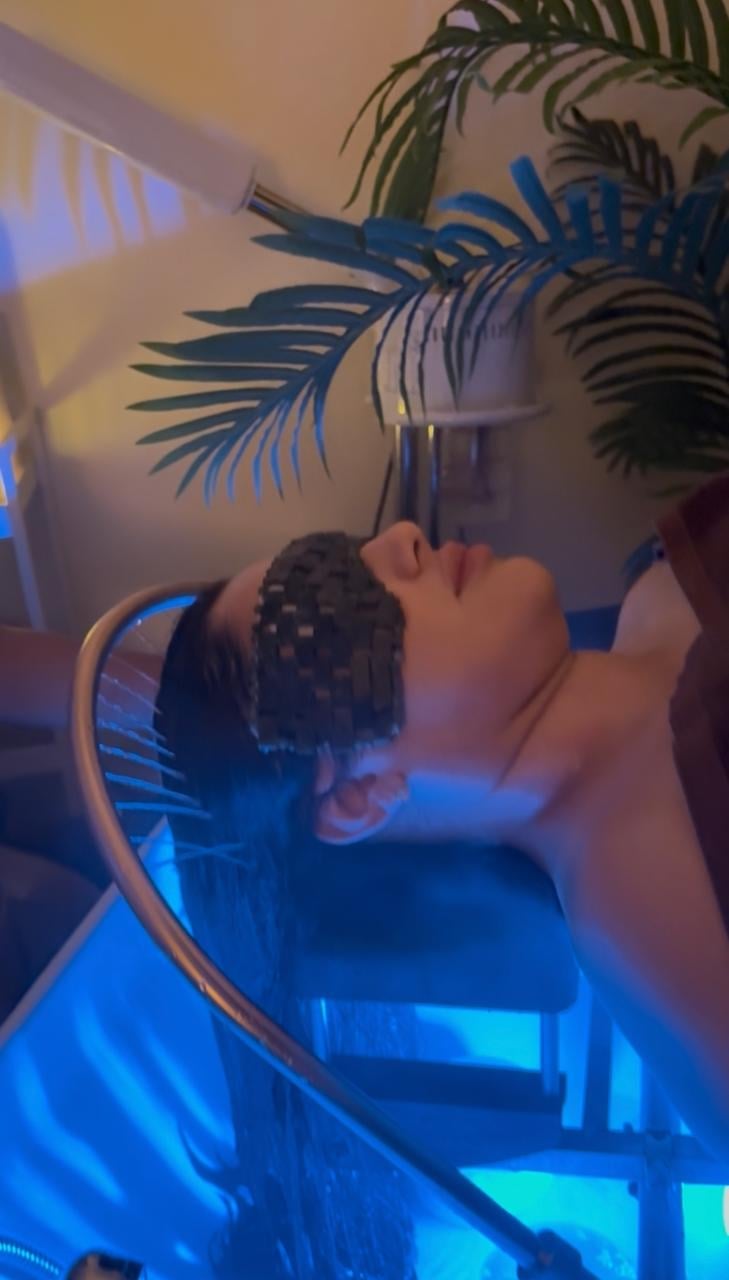 Person with braided hair looking up at decorative palm frond wall art illuminated by blue neon lighting