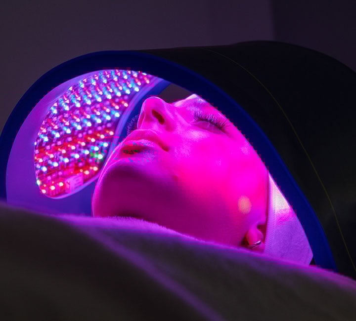 Neon pink and purple LED light therapy device with illuminated panel against dark background