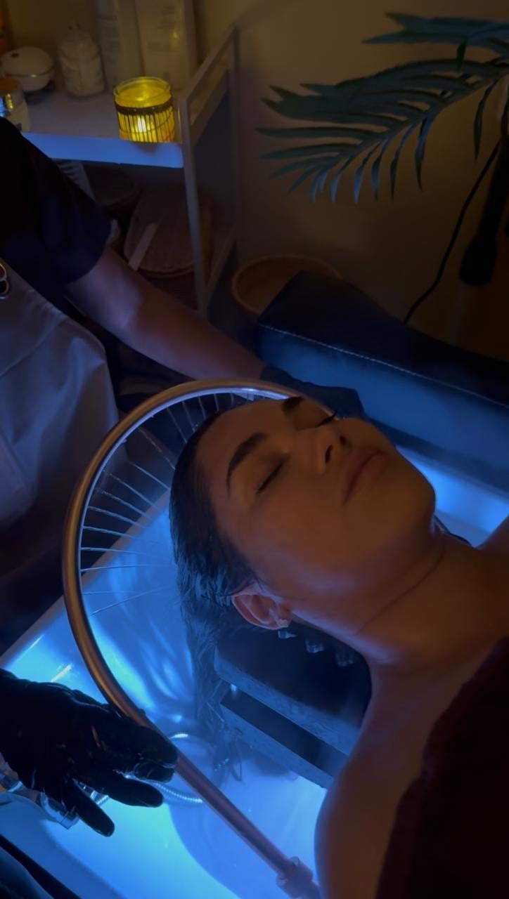 Person lying back in blue LED light therapy bed with eyes closed during skin treatment session