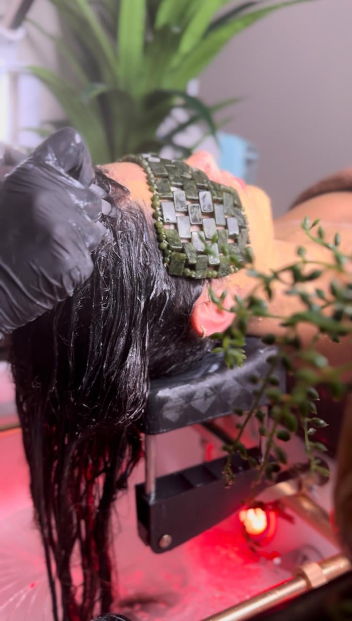 Black bird figurine with moss-covered body and wings surrounded by small green plants under red lighting